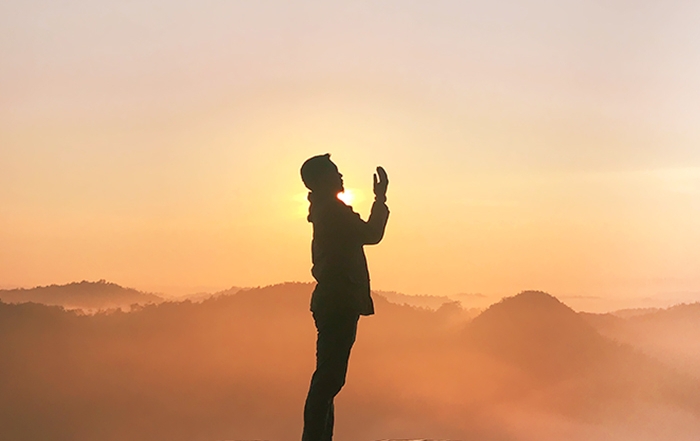 Muslim man supplicating on a high spot with mountains in the background.