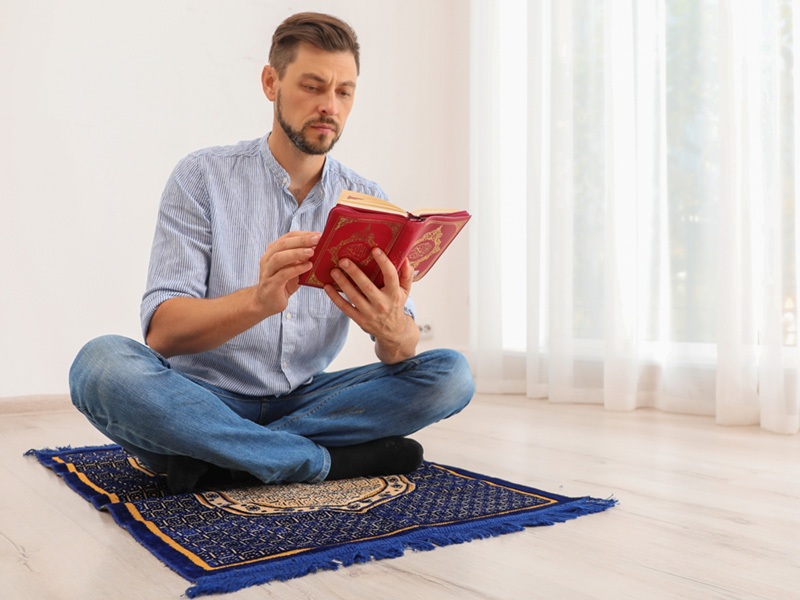 Muslim man reading Quran on a prayer rug